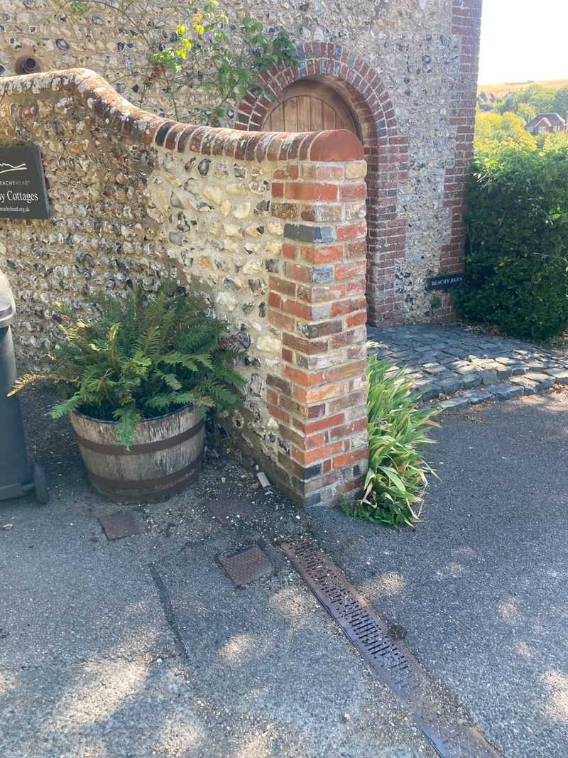 A brick and flint wall with a brick-arched doorway and a planted barrel