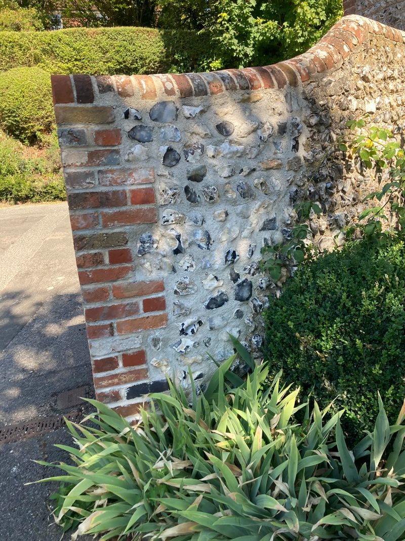 A curved brick coping over a brick quoin where a flint wall steps down