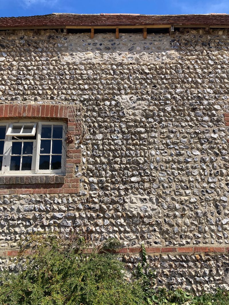 Coursed flint with brick bands and a timber casement window