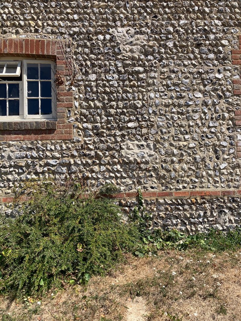 A coursed flint elevation with a brick-dressed window and a brick band