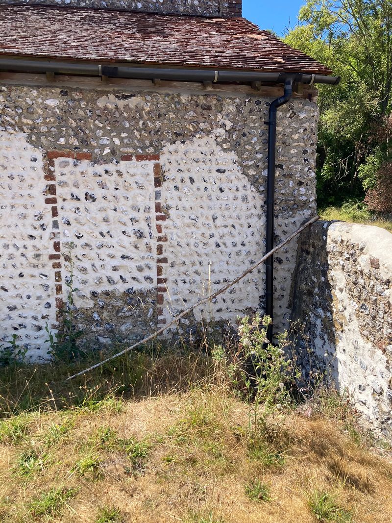A flint elevation with a brick-outlined infilled doorway beneath a tiled roof