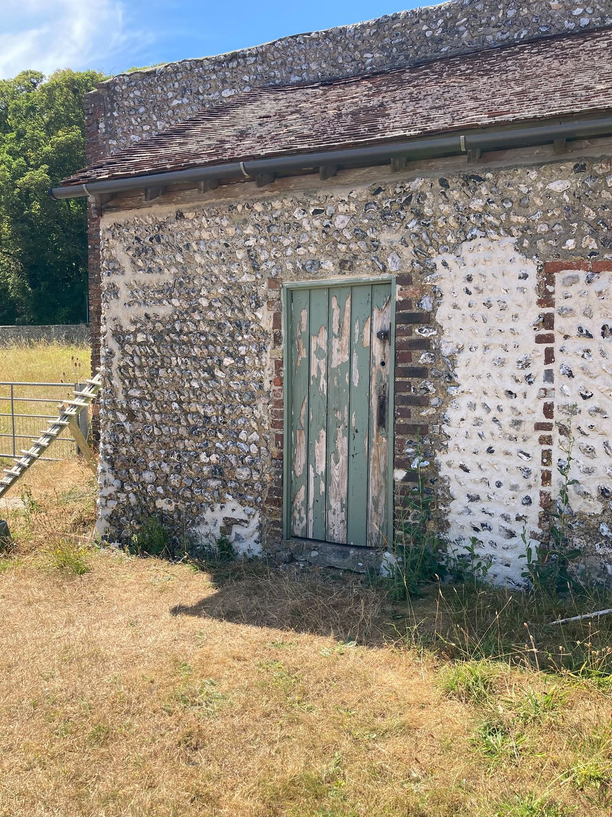 A flint building with brick dressings and a painted green timber door