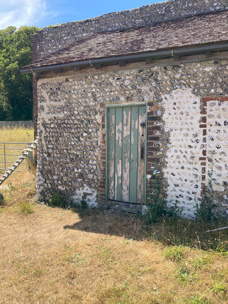 A flint building with brick dressings and a painted green timber door