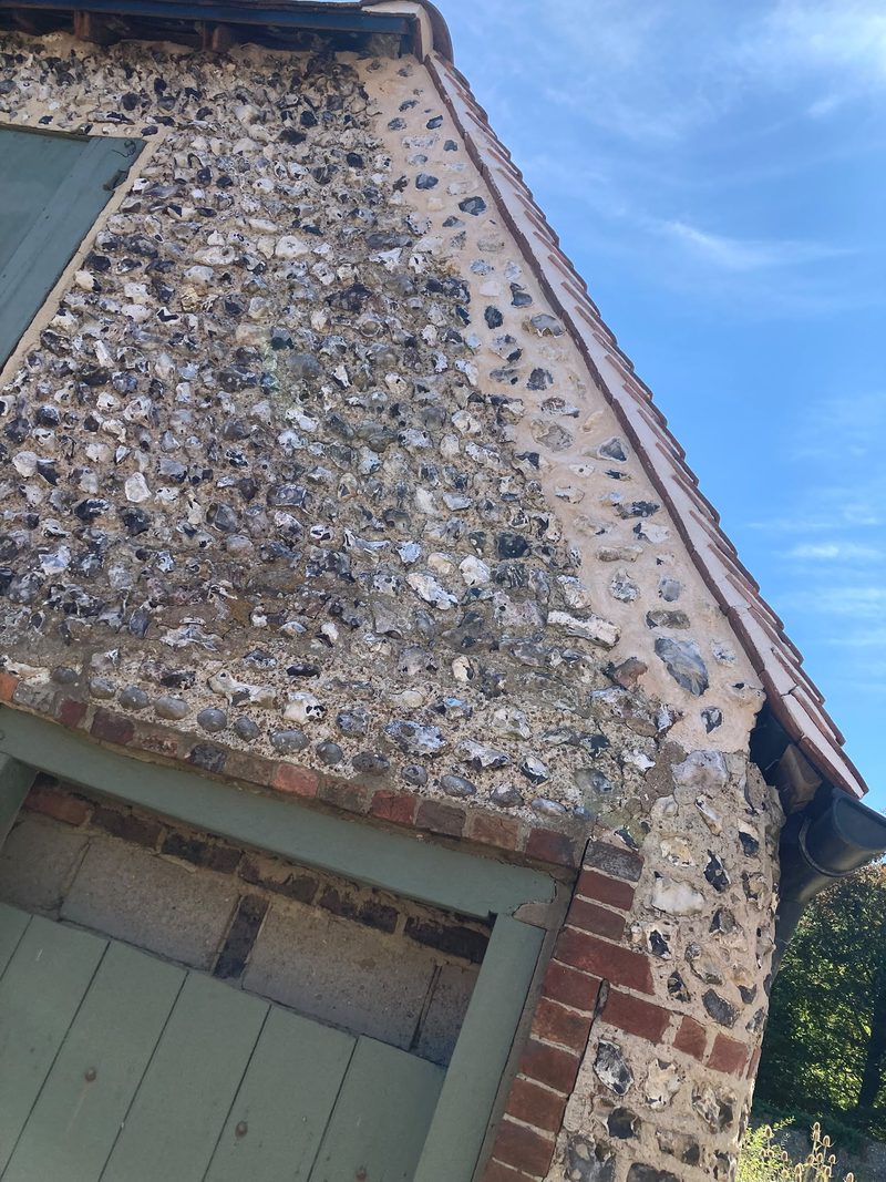 A flint gable and eaves with a green door beneath, seen from below