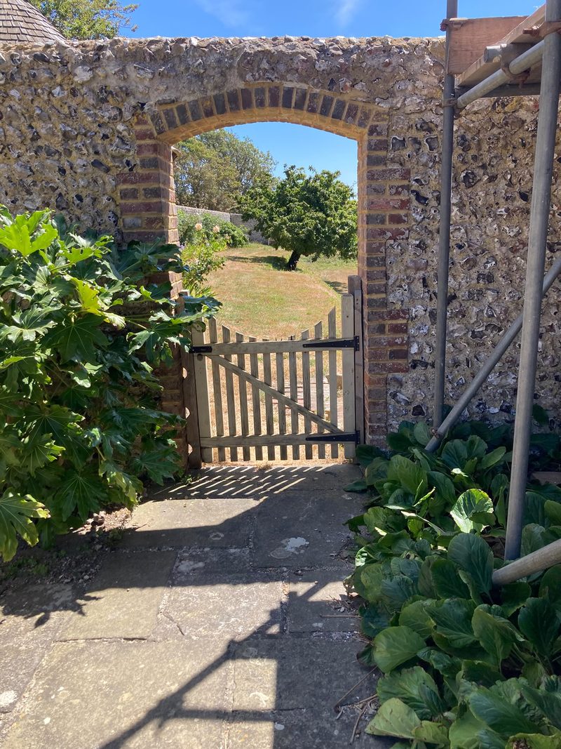 A timber garden gate set between flint piers under a brick arch