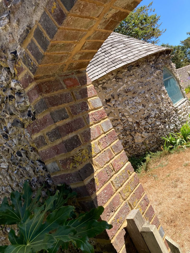 A brick arch springing from a flint pier, with a tiled roof beyond